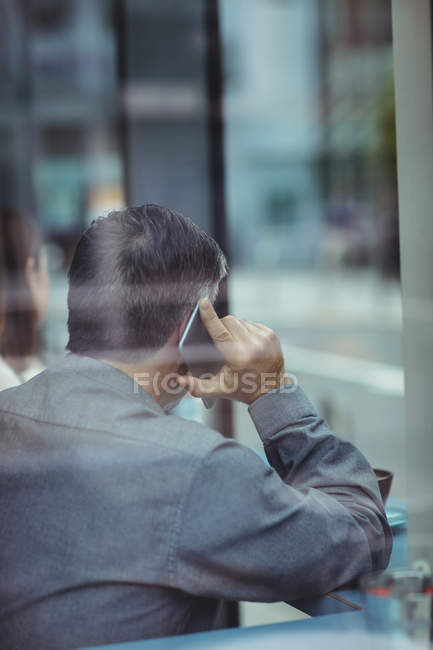 Rückansicht eines Mannes, der in der Cafeteria mit dem Handy spricht — Stockfoto
