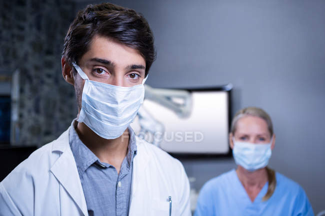 Retrato de dentista e assistente dentário usando máscaras cirúrgicas na clínica odontológica — Fotografia de Stock