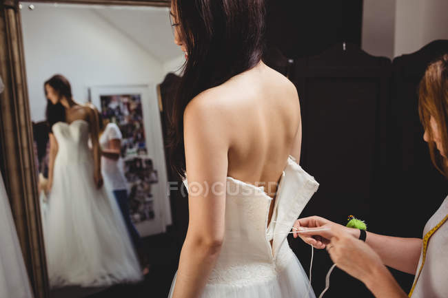 Mulher tentando no vestido de noiva em estúdio com a ajuda do designer criativo — Fotografia de Stock