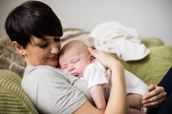 Madre che tiene il bambino mentre dorme in soggiorno a casa — Foto stock