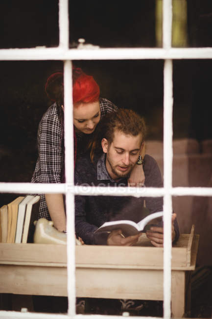 Jovem casal leitura romance em casa visto através de vidro da janela — Fotografia de Stock