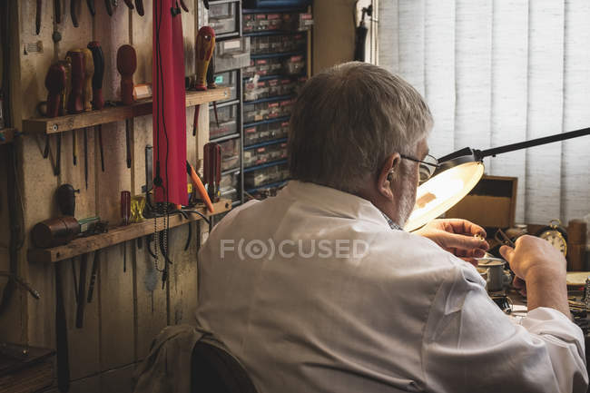 Задний вид на горолога, ремонтирующего часы в мастерской — стоковое фото