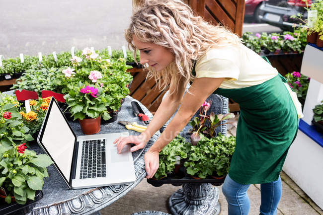Fleuriste féminine utilisant un ordinateur portable dans le centre de jardin — Photo de stock