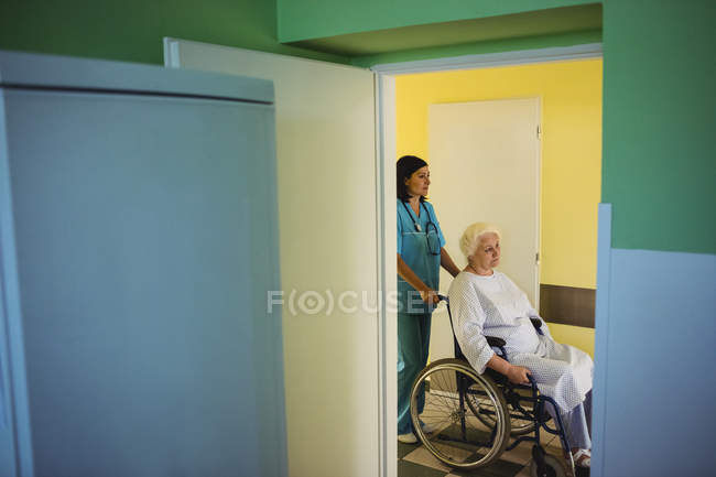 Медсестра толкает пожилого пациента на инвалидном кресле в больнице — стоковое фото
