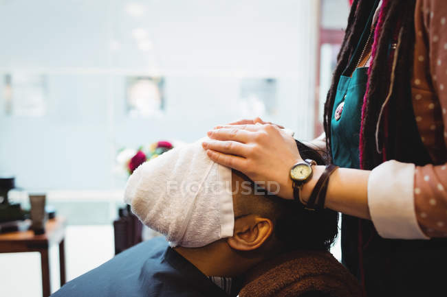 Barbeiro aplicando toalha quente no rosto do cliente na barbearia — Fotografia de Stock