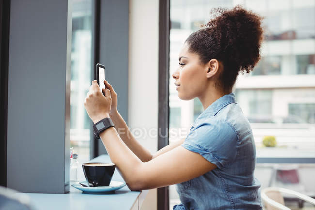 Вид сбоку женщины, использующей телефон во время сидения в ресторане — стоковое фото