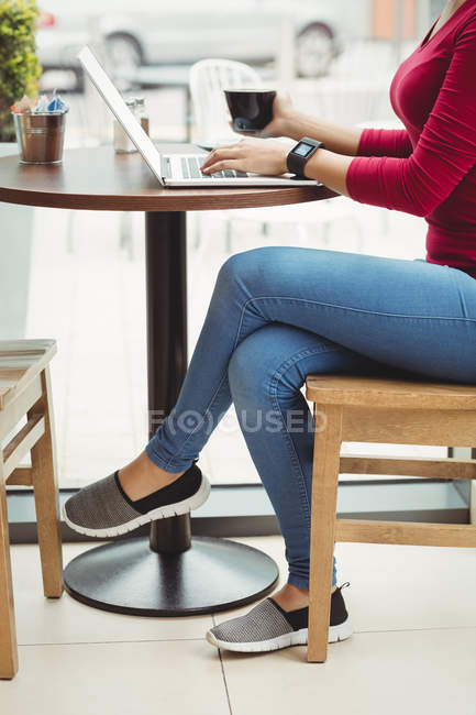 Sección baja de la mujer que usa el ordenador portátil mientras está sentado en el restaurante - foto de stock