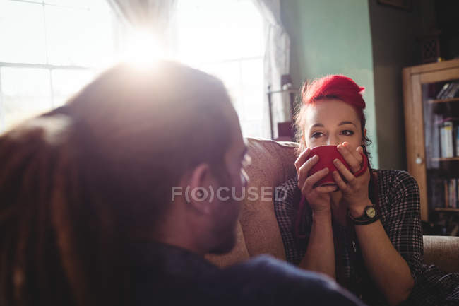 Woman drinking coffee while sitting on sofa by man at home — Stock Photo