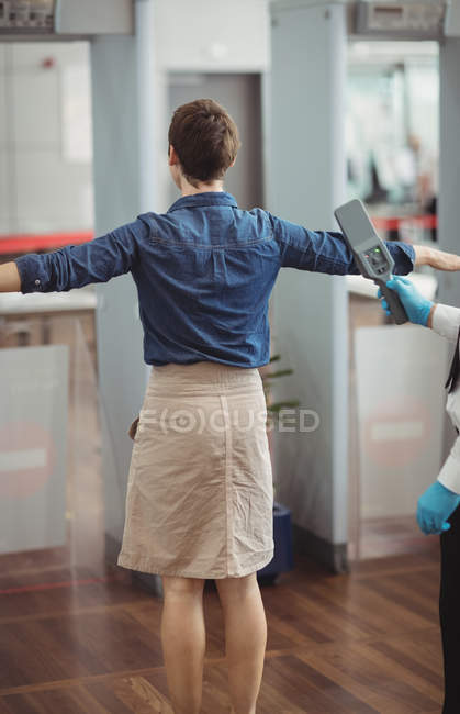 Airport security officer using a hand held metal detector to check a passenger in airport — Stock Photo