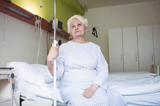 Thoughtful senior woman sitting on bed in hospital — Stock Photo