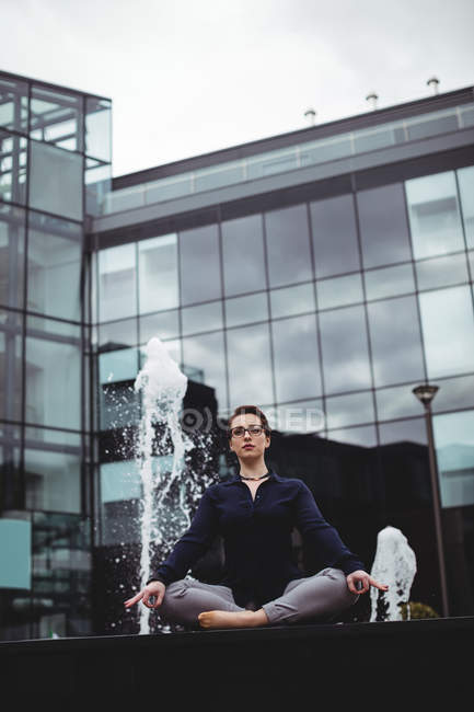 Full length of businesswoman in lotus position against office building — Stock Photo