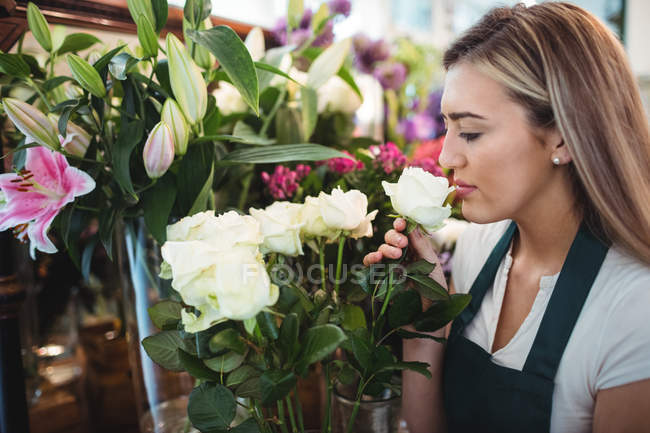 Florista feminino cheirando flor em sua loja de flores — Fotografia de Stock