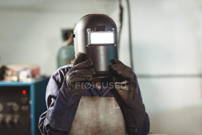 Welder holding welding helmet in workshop — Stock Photo