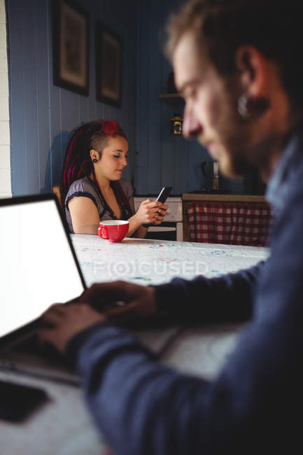 Молодий чоловік використовує ноутбук, коли жінка сидить на задньому плані вдома — стокове фото