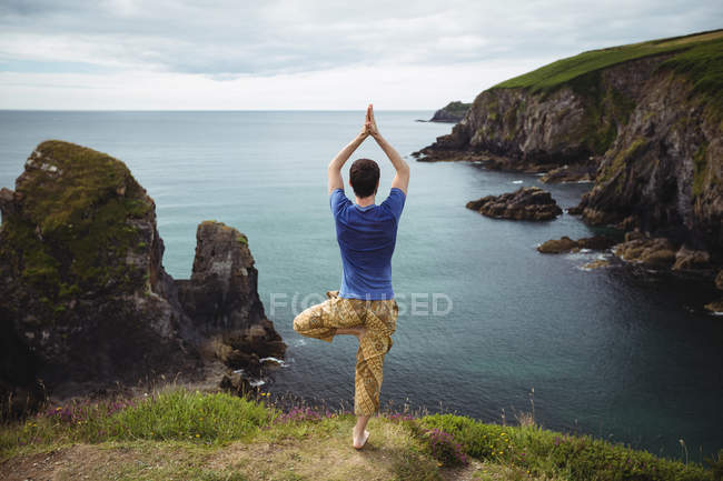 Vista trasera del hombre realizando yoga en el acantilado - foto de stock