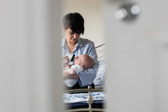 Mother feeding baby with milk bottle in bedroom at home — Stock Photo