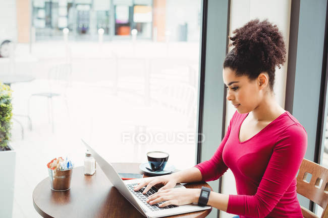 Mujer bonita usando el ordenador portátil mientras está sentado en el restaurante - foto de stock