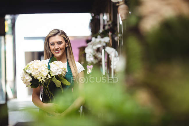 Portrait of female florist holding bunch of flowers at her flower shop — Stock Photo