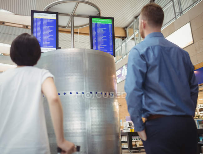 Travellers looking at departure and arrival screen boards displays in airport — Stock Photo