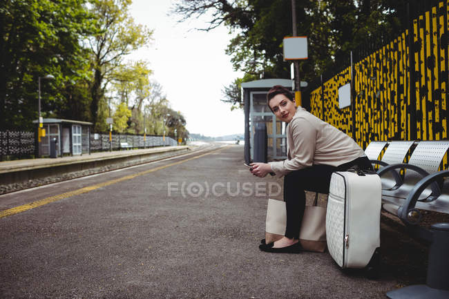 Повна довжина красивої жінки, що сидить на лавці на залізничній станції — стокове фото
