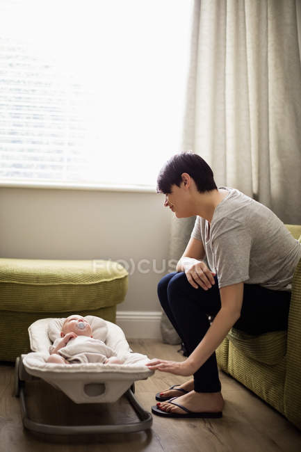 Mother sitting on sofa and looking at baby in living room at home — Stock Photo