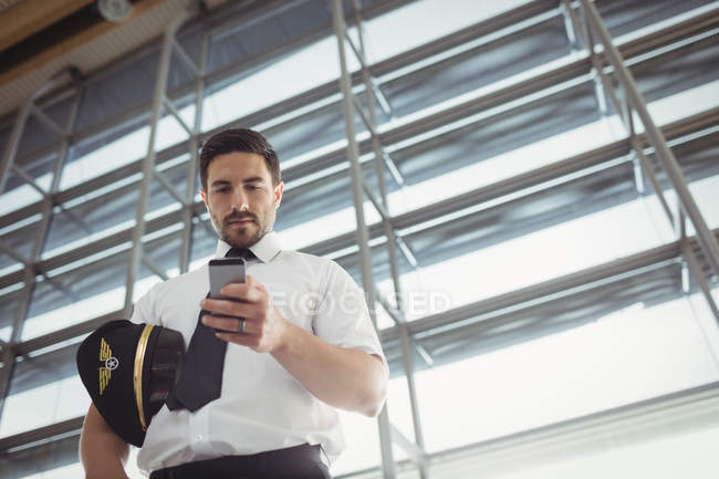 Pilote utilisant un téléphone portable dans la zone d'attente au terminal de l'aéroport — Photo de stock