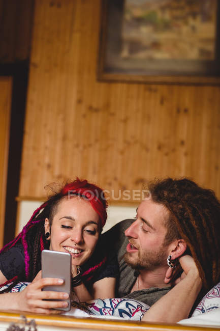Joyeux jeune couple hipster utilisant le téléphone mobile sur le lit à la maison — Photo de stock