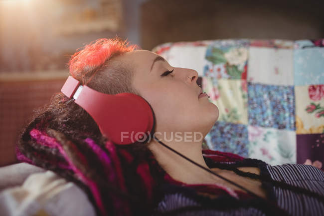 Молода жінка слухає музику, розслабляючись на дивані вдома — стокове фото