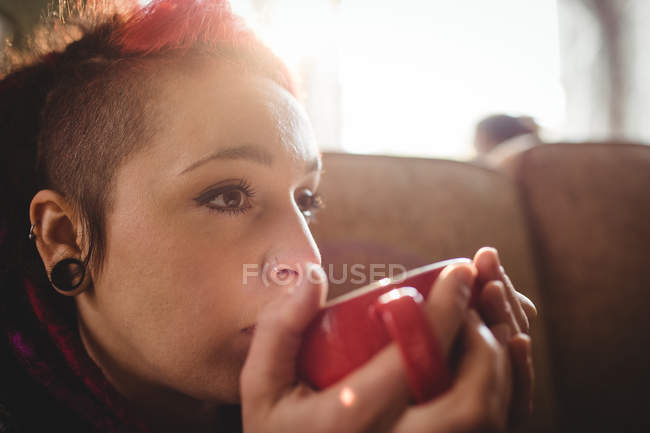 Молода жінка п'є каву, сидячи на дивані вдома — стокове фото