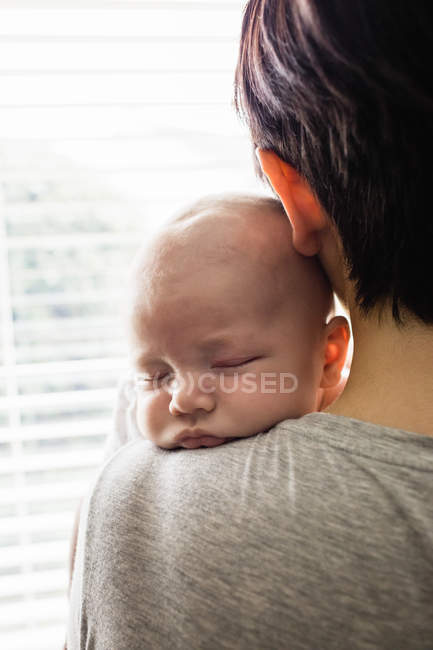 Visão traseira da mãe segurando seu bebê e olhando através da janela em casa — Fotografia de Stock