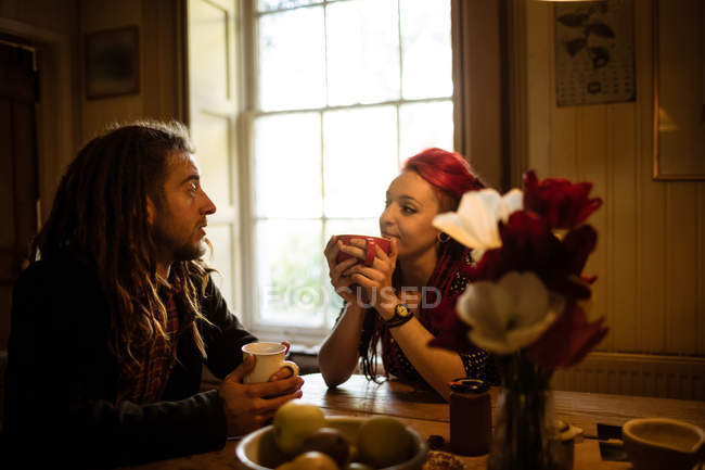 Молода пара говорить, маючи каву за столом в будинку — стокове фото