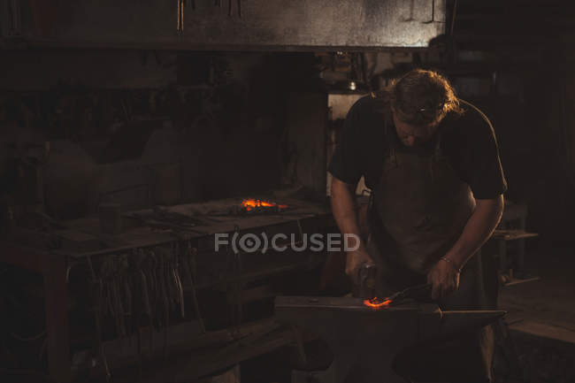 Herrero trabajando en una varilla de hierro calentada en el taller - foto de stock