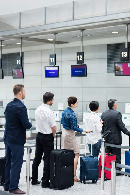 Pasajeros esperando en cola en un mostrador de facturación con equipaje dentro de la terminal del aeropuerto - foto de stock