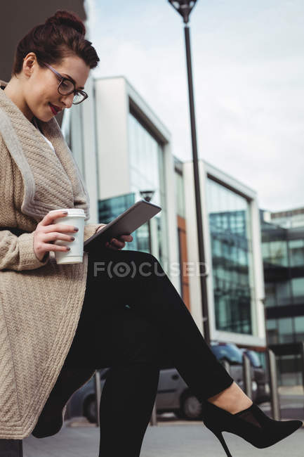 Молода жінка використовує цифровий планшет, тримаючи одноразову чашку проти будівництва — стокове фото
