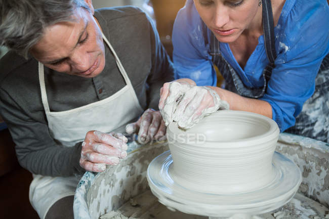 Alfarero masculino asistiendo alfarero femenino en taller de cerámica - foto de stock