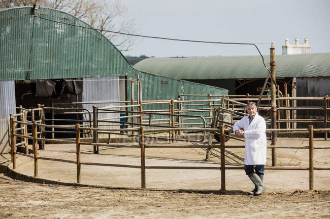 Full length of vet leaning on fence against barn — Stock Photo