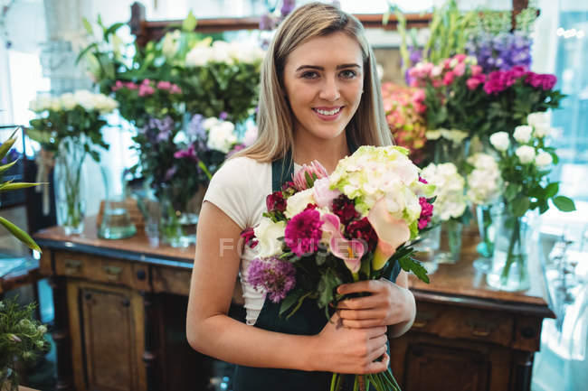 Portrait of female florist holding bunch of flowers at her flower shop — Stock Photo