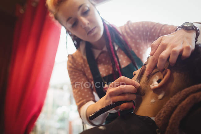 Man getting his beard shaved with razor in a barber shop — Stock Photo