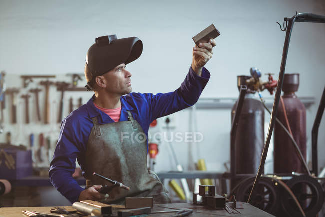 Чоловік зварювальник вивчає шматок металу в майстерні — стокове фото