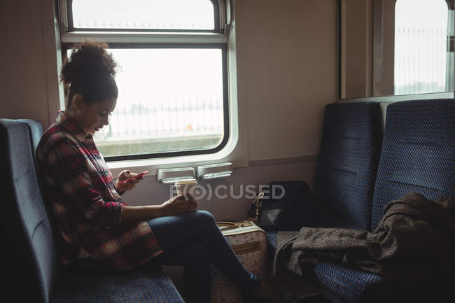 Vista lateral de la mujer joven usando el teléfono mientras está sentada en el tren - foto de stock