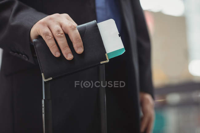 Mid section of passenger holding boarding pass and passport in airport terminal — Stock Photo
