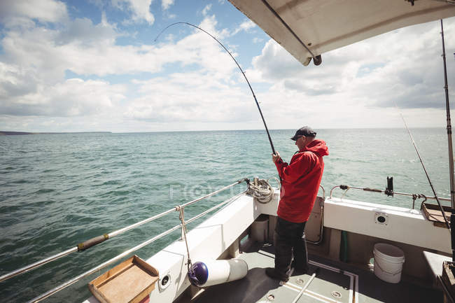 Vista lateral de la pesca del pescador con caña de pescar del barco - foto de stock