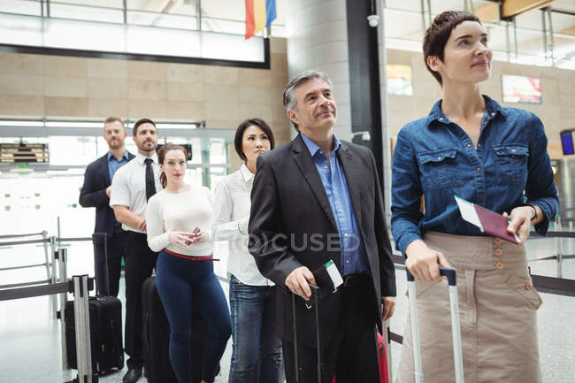 Pasajeros esperando en cola en un mostrador de facturación con equipaje dentro de la terminal del aeropuerto - foto de stock