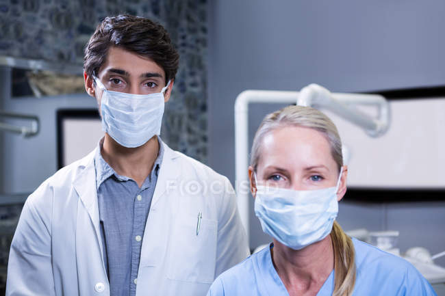 Портрет зубного врача и ассистента стоматолога в хирургических масках в стоматологической клинике — стоковое фото