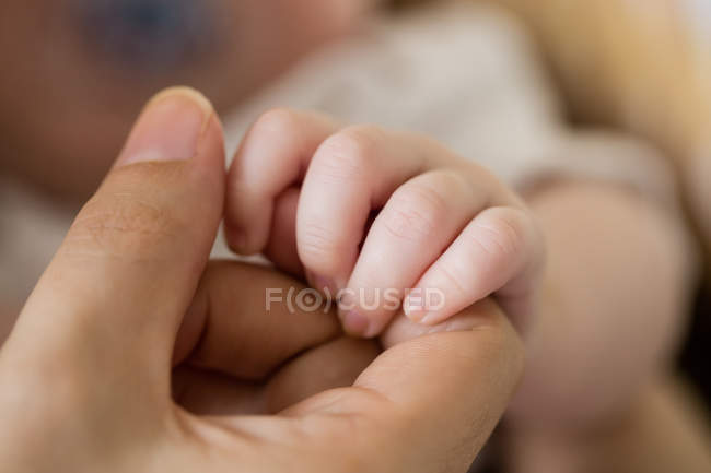 Image recadrée de bébé tenant la main mère à la maison — Photo de stock