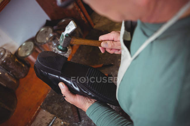 Zapatero martillando un zapato en el taller - foto de stock