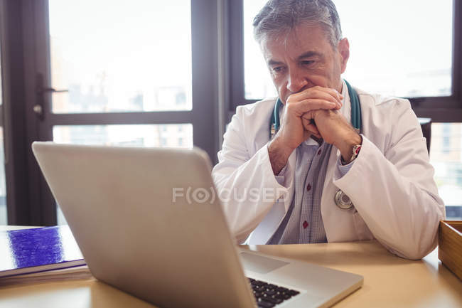 Doctor usando laptop en su escritorio en el hospital - foto de stock