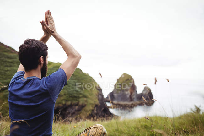 Vue arrière de l'homme effectuant le yoga sur la falaise — Photo de stock