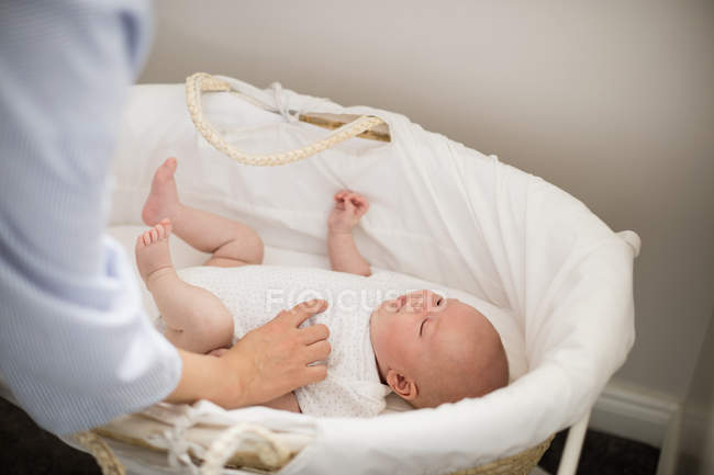 Imagen recortada de la madre tocando al bebé durmiendo en la cesta en casa - foto de stock