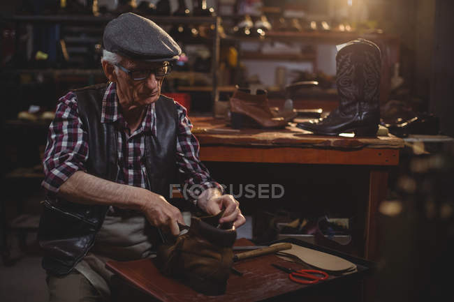 Shoemaker in cap repairing a shoe in workshop — Stock Photo